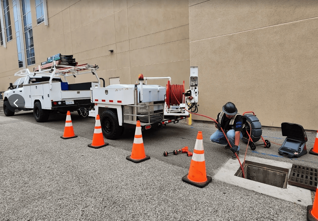 Armor service truck and hydro jetting trailer at a commercial storm drain while a technician works at the open drain